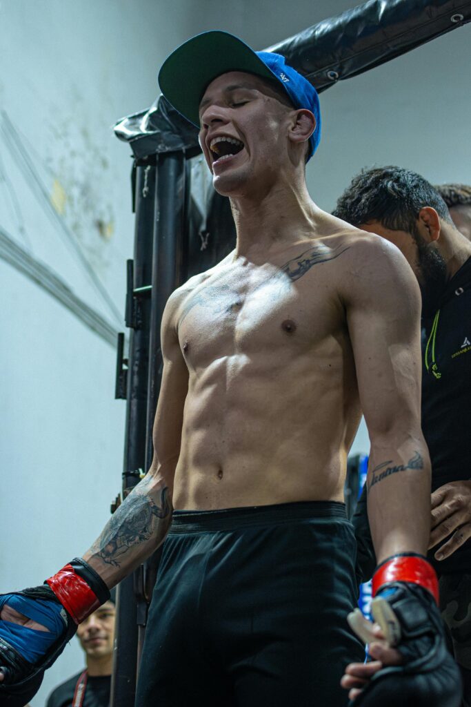 A mixed martial artist celebrating his victory indoors with enthusiasm, showcasing his athletic physique.